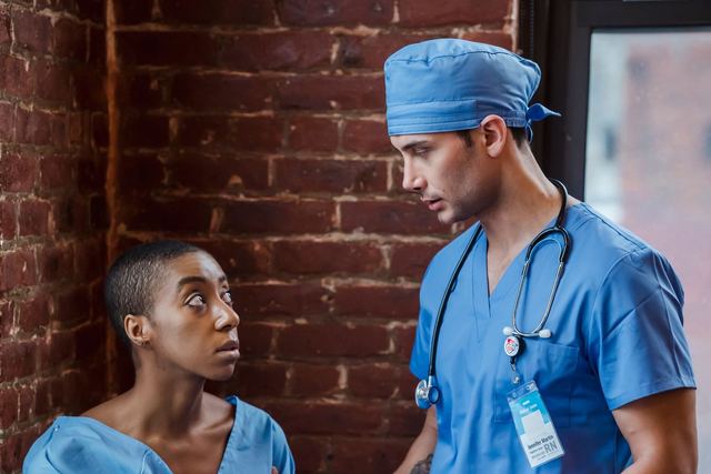 Calm doctor in blue uniform standing and talking diagnosis to African American woman patient in hallway of clinic in daytime