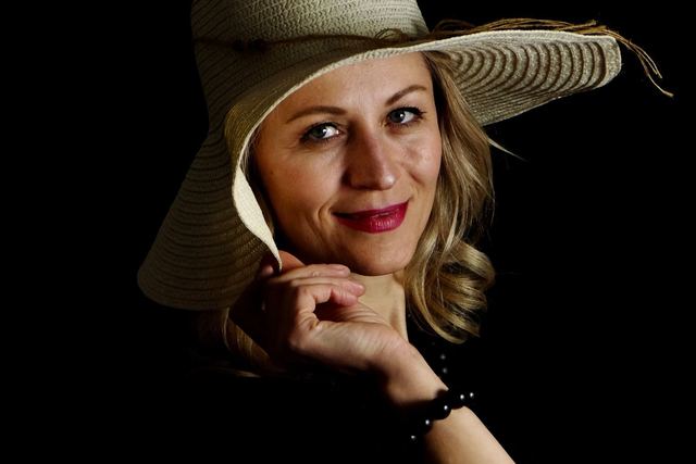 Chic portrait of a smiling woman in a stylish hat, with a black background, captured in studio.