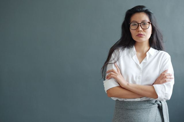 Confident woman in white shirt with arms crossed, wearing glasses, serious expression.