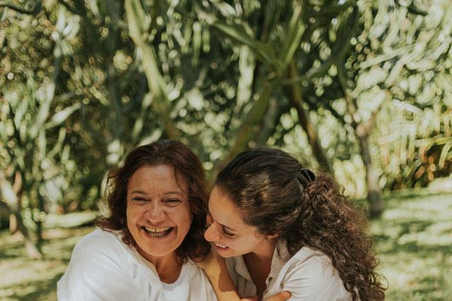 A mother and daughter sharing a joyful moment outdoors surrounded by greenery.