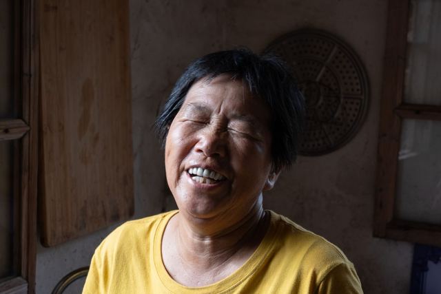 Elderly woman laughing joyfully, captured indoors in warm light.