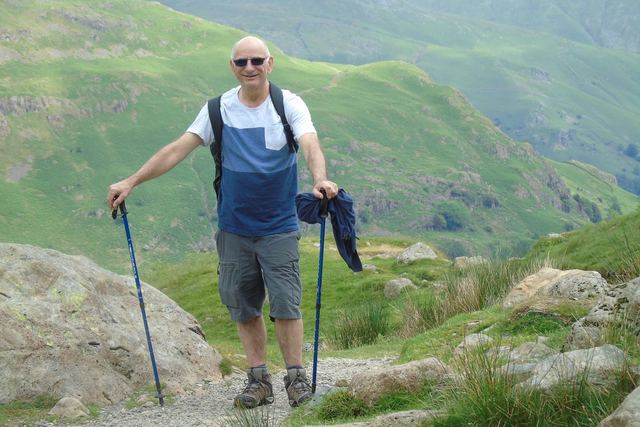 Elderly man hiking in the English mountains with trekking poles on a sunny day.