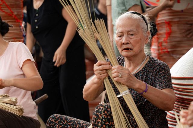 Elderly woman crafting conical hats in Hà Nội, showcasing tradition and culture.