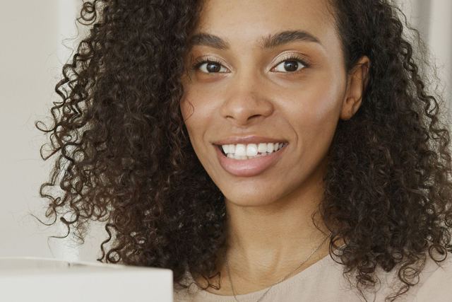 Confident woman with curly hair smiling amidst packages, symbolizing entrepreneurial success.