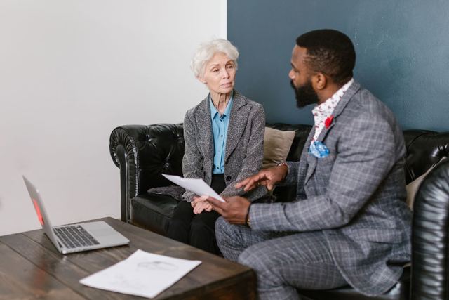 An elderly woman and a man in a professional meeting discussing documents indoors.