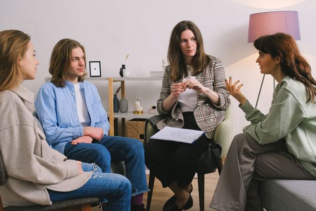 Female in casual clothes sitting on sofa and talking with psychologist and other people in group