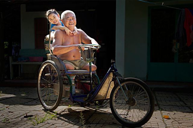Elderly man and cheerful child enjoying a tricycle ride outdoors in sunlight.