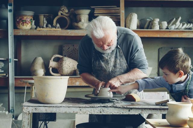 An elderly man and a child working together on clay pottery in an artisan workshop.