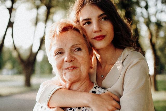 A touching moment between a mother and daughter embracing in a sunlit park setting.