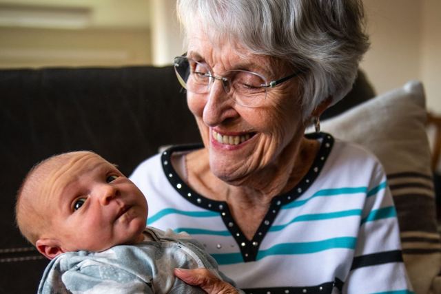 A senior woman lovingly holds her newborn grandchild indoors, conveying warmth and family bonds.