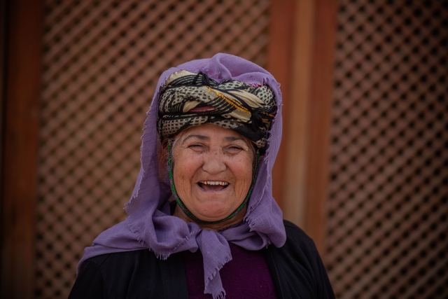 Elderly woman laughing in a traditional headscarf with a vibrant smile, outdoors.