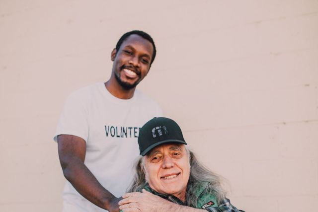 Happy volunteer with elderly man in wheelchair, showcasing kindness and community support.