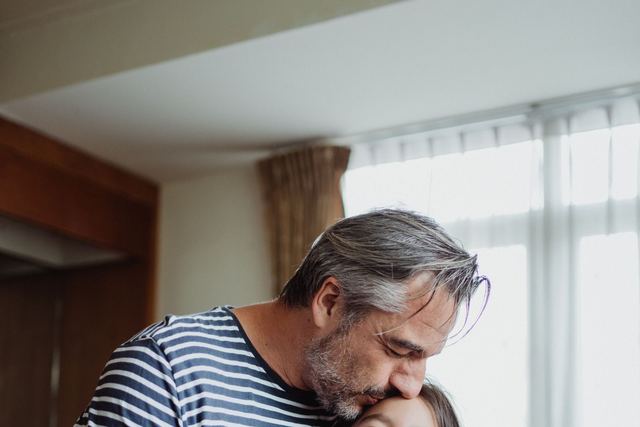 Adorable moment of a father kissing his daughter holding a cupcake indoors.