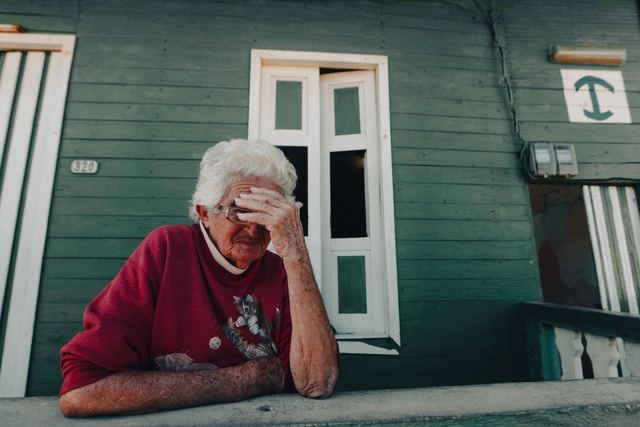 Pensive elderly woman sitting on a porch, evoking feelings of reflection and solitude.