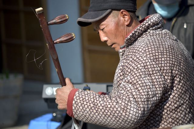 Close-up of a man playing the Chinese erhu outdoors, showcasing cultural music traditions.