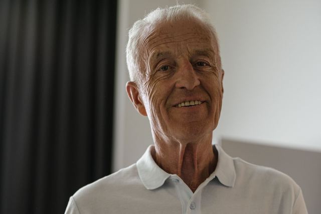 Elderly man happily holding a bowl of fresh vegetables indoors, promoting healthy lifestyle.
