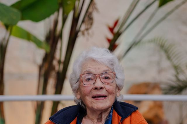 Elderly woman in a wheelchair with plants in the background.