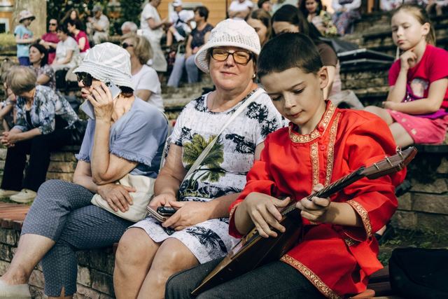 Young boy in traditional attire plays balalaika at outdoor cultural event.
