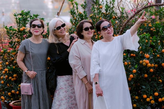 Four senior women smiling and enjoying their time outdoors among lush citrus trees.