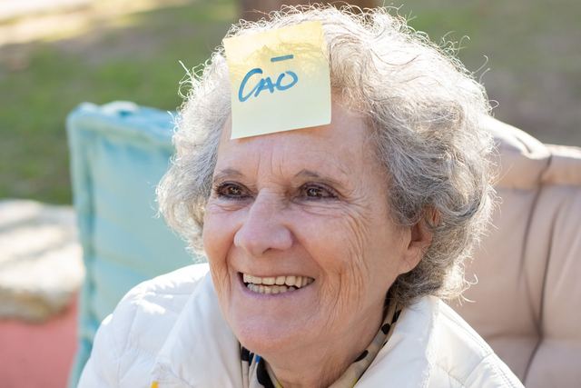 Happy elderly woman with a sticky note on her forehead enjoys a sunny day outside.