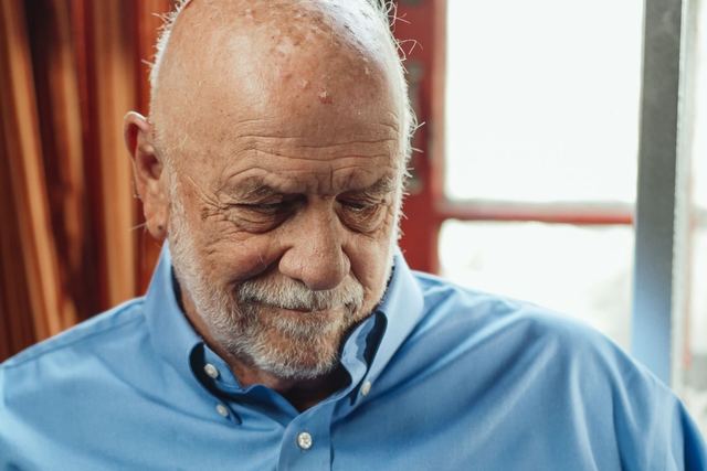 Senior man in blue shirt holding a photo frame, reflecting thoughtfully indoors.