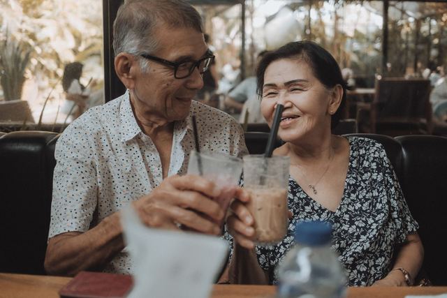 Happy senior couple sharing a moment with iced beverages in a cozy cafe setting.