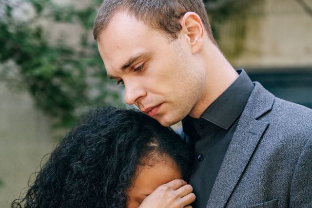 A couple embracing in comfort during a moment of grief, outdoors with a somber tone.