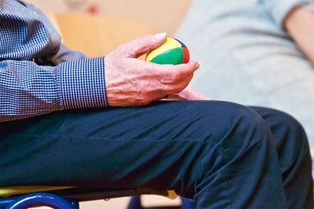 Elderly man holding a colorful therapy ball indoors, promoting relaxation and health.