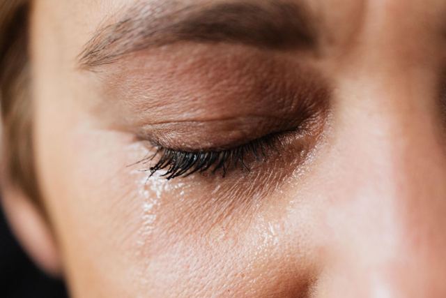 Closeup of crop sad adult lady with natural makeup having problems and crying alone