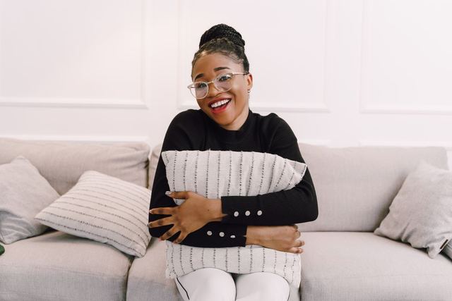 Happy woman with glasses hugging a pillow on a couch, exuding warmth and joy.