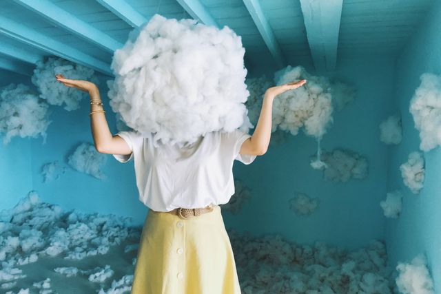 Whimsical art piece with a person having a cloud as a head in a blue room filled with clouds.