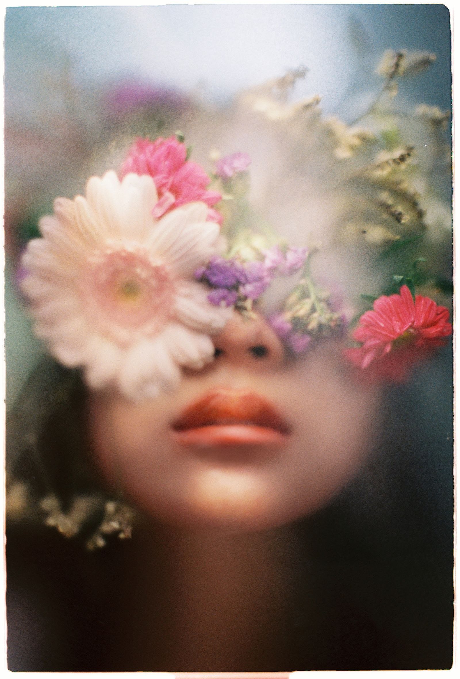Romantic portrait with colorful flowers obscuring a woman's face, creating an ethereal effect.